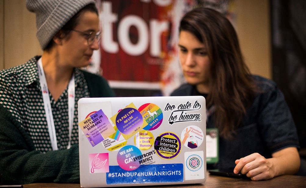 Two activists speak behind a laptop with LGBTI speakers