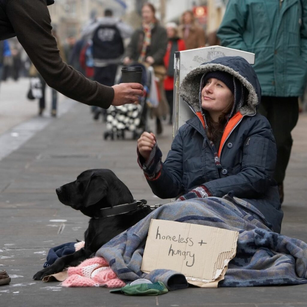 person giving a cup to a young homeless person