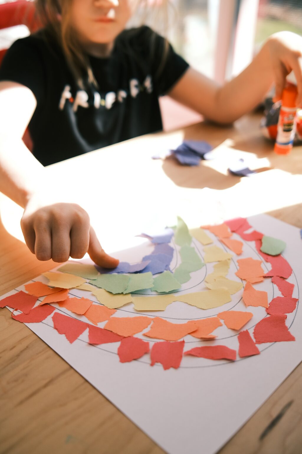 A child designing a rainbow map with colored papers