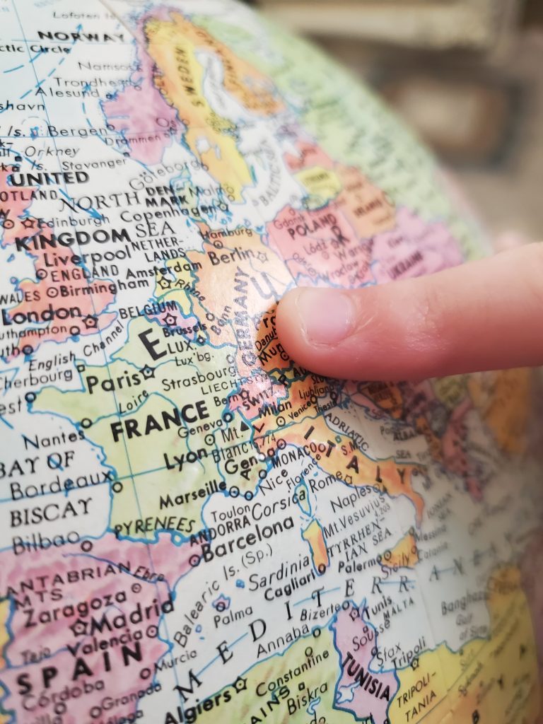 A finger points to a country in Europe on a globe