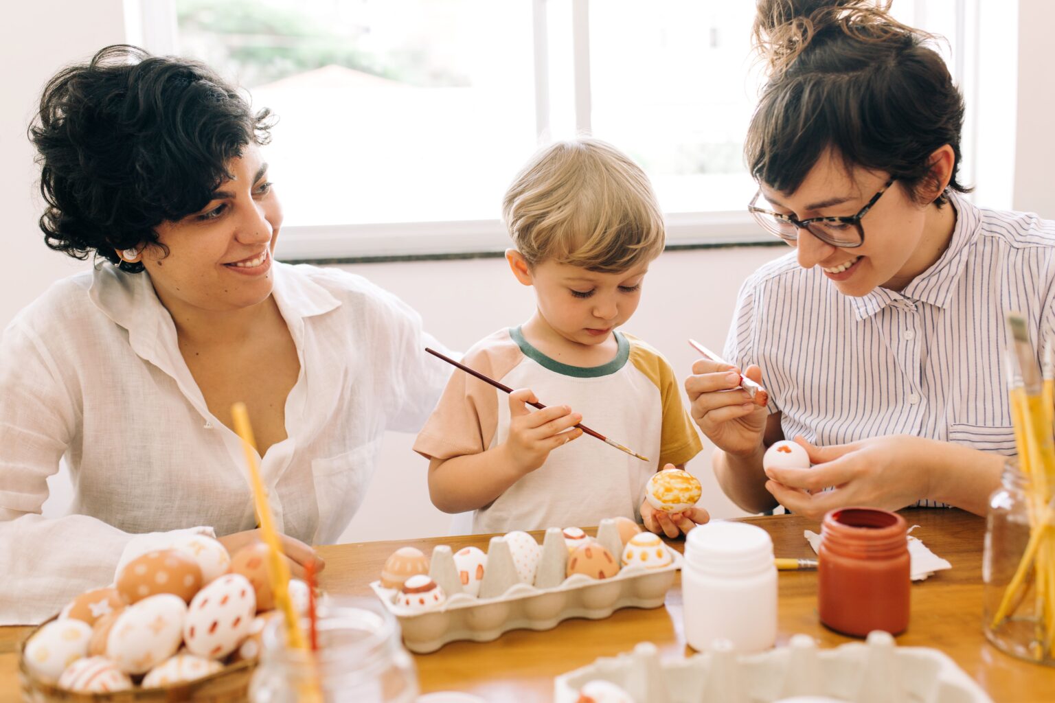 Two mothers in white shirts and their child paint eggs