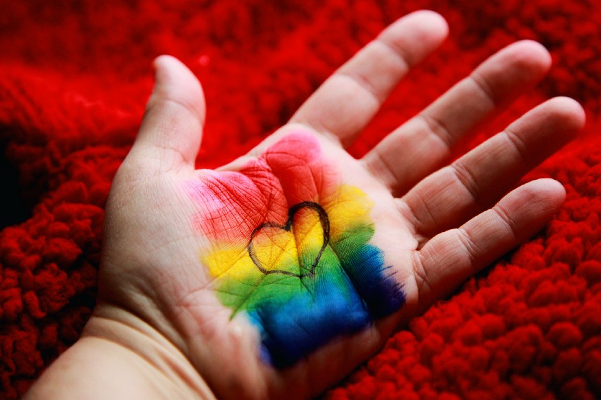 An open hand with a heart and rainbow colors and a red background