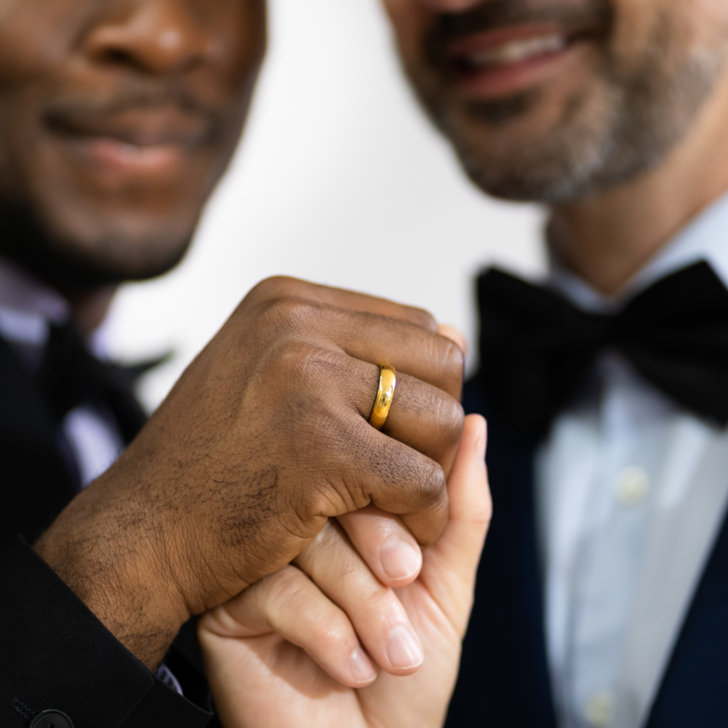 Two grooms hold hands, showing their wedding rings