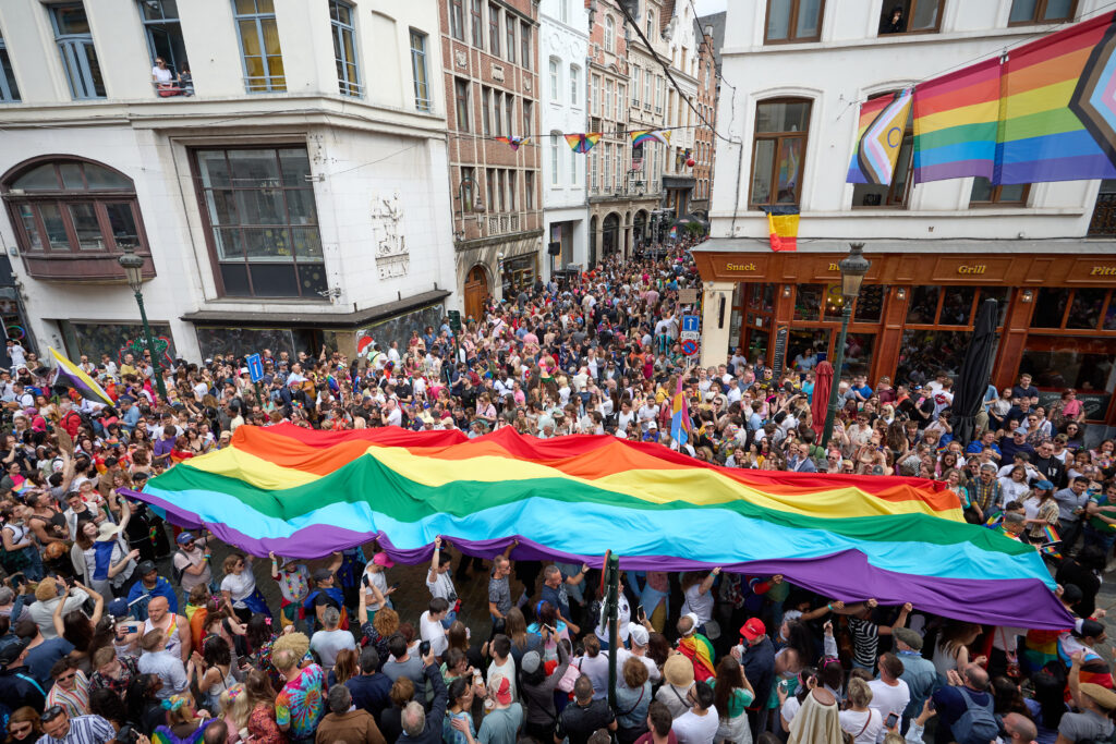 A large crowd holding a rainbow flag above their heads in the streets of Brussels