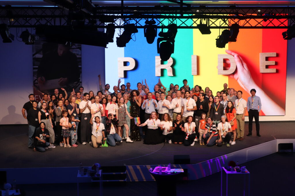 Toyota employees at their Pride event with La Diva Live on stage against a rainbow backdrop and Pride lettering