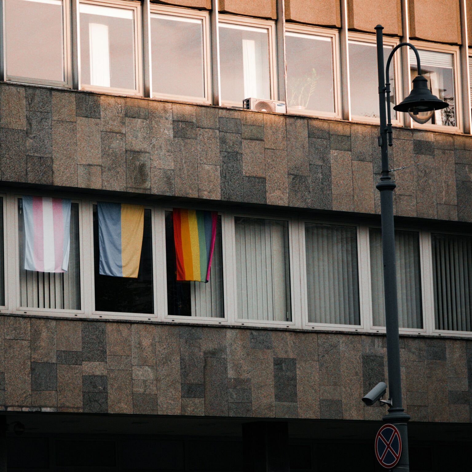 A transgender, Ukraine, and rainbow flag hanging from windows of a building.
