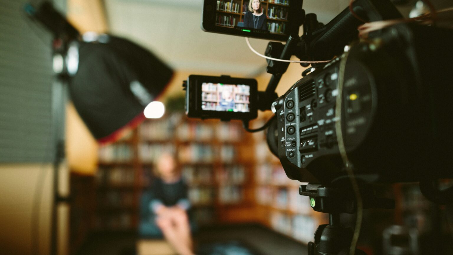 A photograph of a TV camera filming a blurred out person.